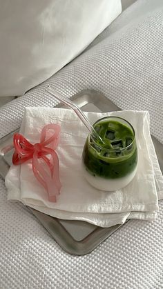 a green drink with a red bow sitting on top of a white napkin next to a spoon