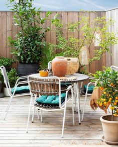 an outdoor table and chairs on a wooden deck with potted trees in the background