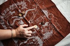 a person is drawing on a piece of cloth with buttons in their left hand and the other hand pointing at it