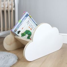 a white cloud shaped book stand with books in it on the floor next to a baby's crib