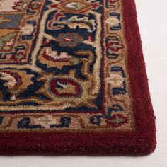 a red rug with an ornate design on the top and bottom, sitting on a white surface