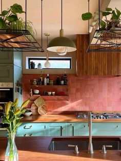 a kitchen with green cabinets and pink tile backsplash, potted plants on the counter