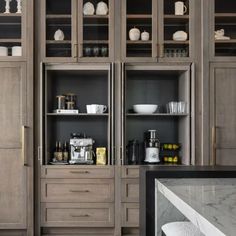 a kitchen with wooden cabinets and marble counter tops, along with white dishes on the shelves