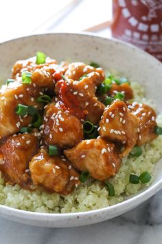 a white bowl filled with rice covered in chicken and sesame seeds on top of it