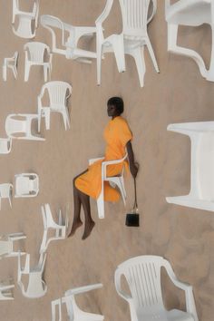 a woman in an orange dress is sitting on a white chair and looking down at the ground