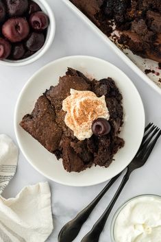 a white plate topped with brownies next to bowls of cherries and whipped cream