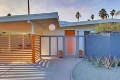 a house with a blue fence and palm trees in the back ground, on a sunny day