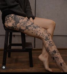 a woman sitting on top of a wooden chair with tattoos on her arm and leg