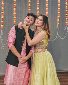 two people standing next to each other in front of a wall decorated with garlands