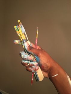 a person's hand holding several different colored paintbrushes in their left hand