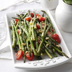 asparagus with tomatoes and almonds on a white plate next to a vase