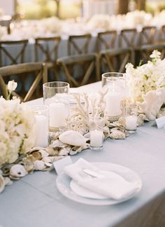 the table is set with white flowers, candles and seashells for an elegant touch