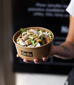 a person holding a bowl with food in it and the words grills written on it