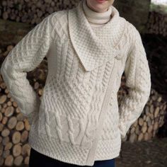 a woman standing in front of stacks of logs wearing a white sweater and black pants