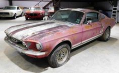 an old mustang sits in a garage with other cars behind it and rusted paint on the hood