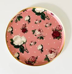 a pink plate with white and red flowers on it, sitting on a table next to a wall