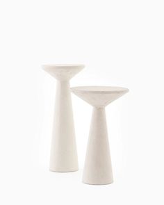 two white vases sitting next to each other on a white surface with no one around them