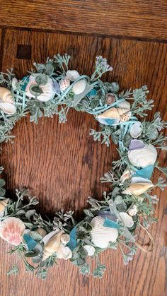 a wreath made out of seashells and greenery on a wooden table top