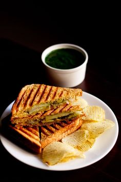 a grilled sandwich and chips on a white plate with a cup of green tea