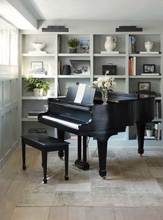 a black piano sitting in the middle of a living room next to a book shelf