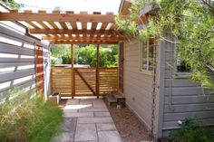 a small backyard with a wooden pergoline and stone walkway leading to the back door