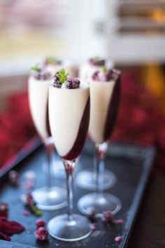 three glasses filled with white wine and garnished with raspberries on a tray