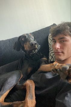 a man laying on top of a black couch next to a brown and black dog