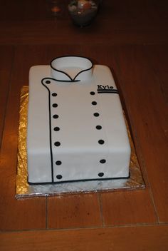 a white cake with black dots on it sitting on top of a wooden table next to a vase