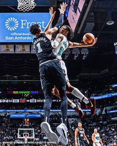 two men playing basketball in front of an audience at a sporting event, one is jumping up to dunk the ball