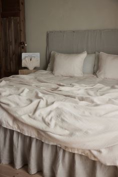 an unmade bed with white linens in a bedroom next to a wooden door