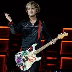 a man holding a guitar on stage with his hands in the air and one hand out