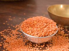 a metal bowl filled with red lentils on top of a wooden table