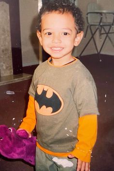 a young boy standing next to a purple stuffed animal