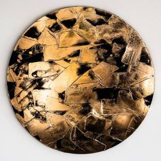 a round gold plate with black and white designs on the top, in front of a white wall