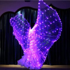 a woman is dancing with purple lights on her body and arms, in front of a black curtain