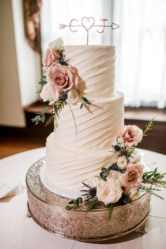 a white wedding cake with pink flowers and an arrow topper is on a silver platter