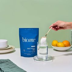 a person scooping sugar into a glass with oranges on the table next to it