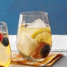 two glasses filled with fruit and ice on top of a cloth covered table next to a blue wall