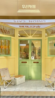 two lawn chairs sitting in front of a yellow building with stained glass doors and windows