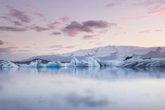 icebergs floating in the water at sunset with mountains in the background and clouds in the sky