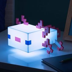 an illuminated box with pink and blue squares on it sitting on a table next to a notebook