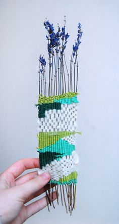 a person holding up a piece of art made out of beaded material and yarn