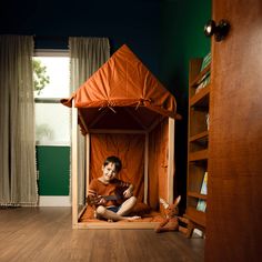 a boy sitting in a wooden bed with an orange tent