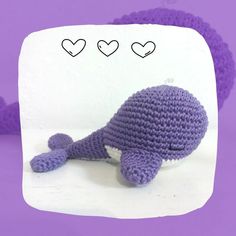 a crocheted stuffed animal laying on top of a purple background with hearts above it