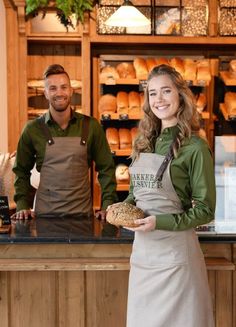 a man and woman in aprons standing behind a counter with bread on the plate