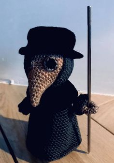 a crocheted stuffed animal wearing a top hat and holding a cane on a wooden table