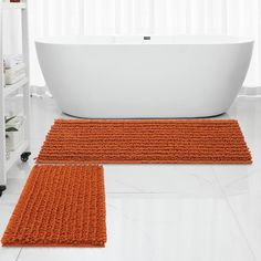 two orange bath mats sitting next to a white tub in a bathroom on the floor