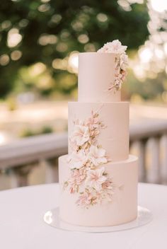 a three tiered wedding cake with pink flowers on the top and bottom, sitting on a table outdoors