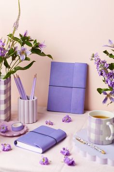 purple flowers are in vases on a table next to notebooks and pencils