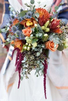 a bride holding a bouquet of flowers and greenery on her wedding day in the fall